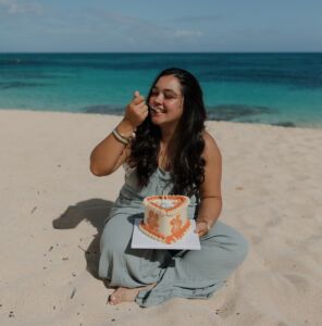 Woman enjoying a custom birthday cake with orange floral buttercream during a beach cake smash photoshoot
